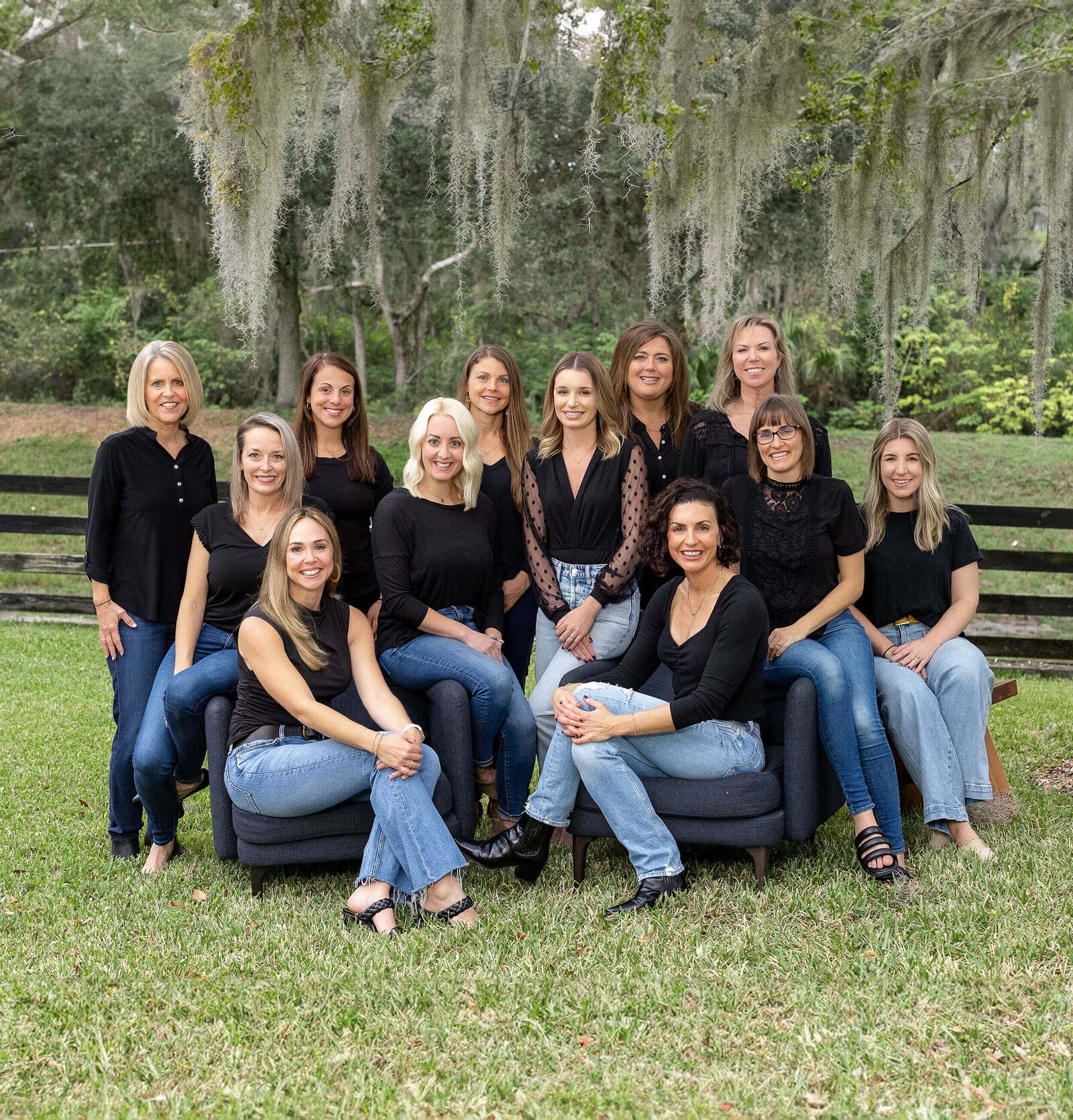 Faithfully Guided Health Center team gathered outdoors, sitting and standing together, wearing coordinated black tops and blue jeans.