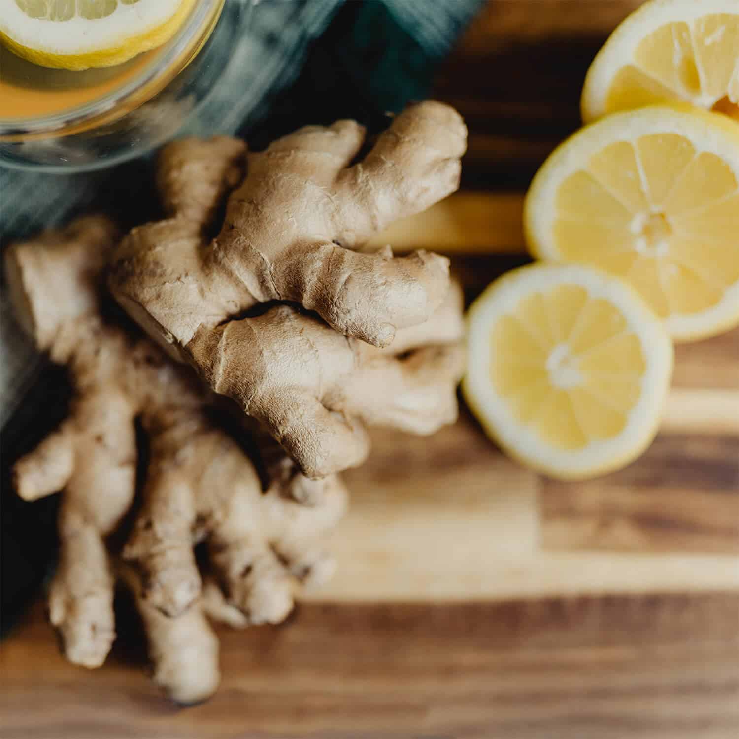Fresh ginger root and sliced lemon on a wooden cutting board, next to a cup of lemon tea—ingredients known for their anti-inflammatory properties.
