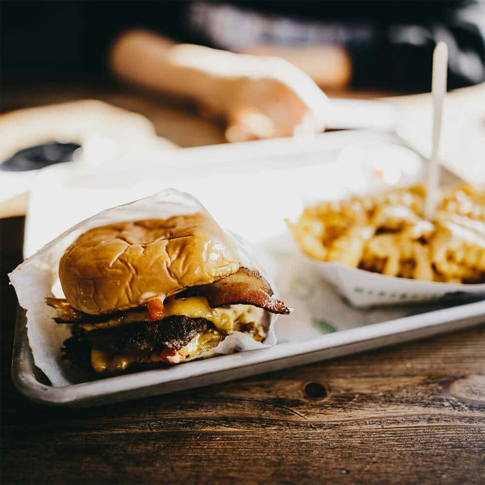 Cheeseburger with bacon and a side of crinkle-cut fries on a tray, representing inflammatory food choices that may worsen autoimmune symptoms.
