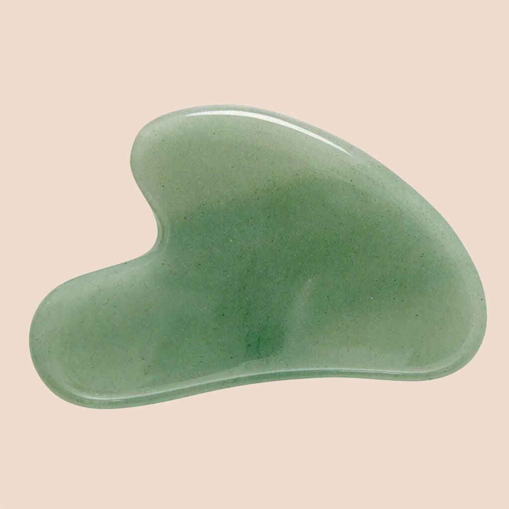 A smooth green jade gua sha facial tool photographed on a soft beige background.