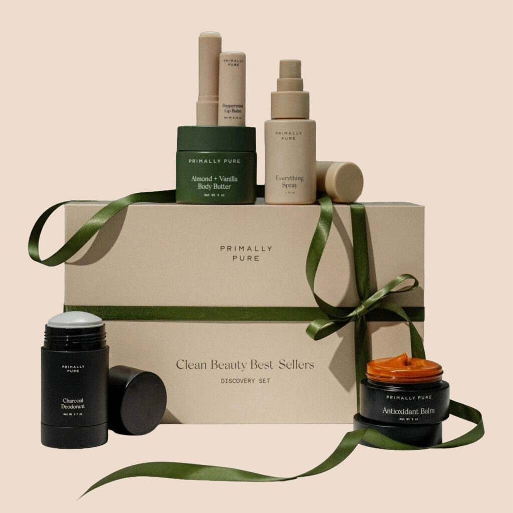 A Primally Pure gift set featuring skincare products arranged on top of a boxed set tied with a green ribbon, with items including deodorant, lip balm, body butter, spray, and antioxidant balm.